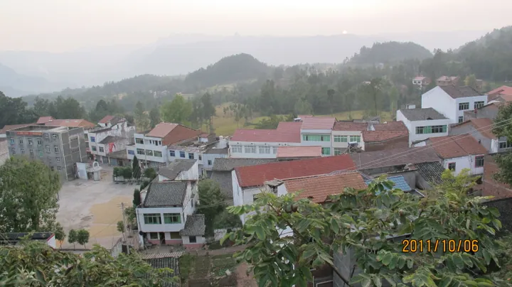 Elevated view of red-roofed village buildings and hills in Miaoya, Wanyuan
