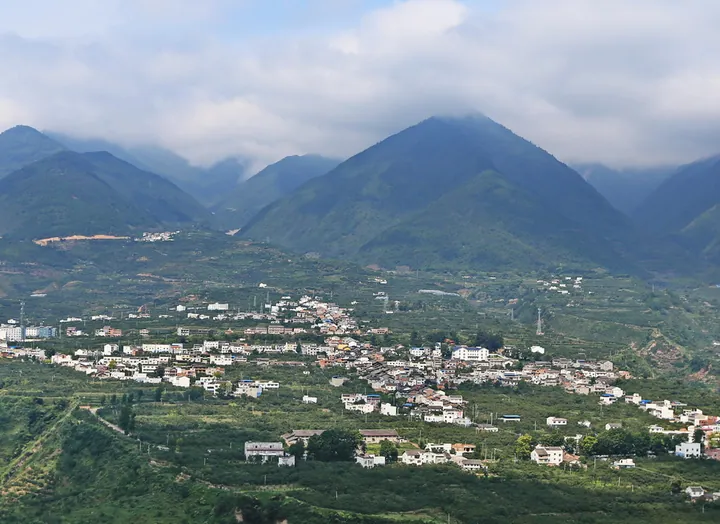 A village spread across a valley floor beneath cloud-capped mountains in Hanyuan County