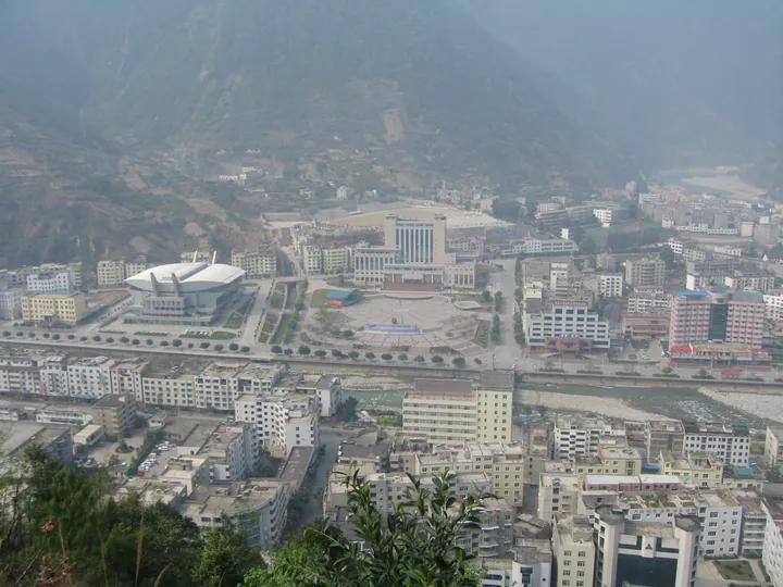 A hazy aerial view of the town of Shimian in a mountain valley, with a stadium and river