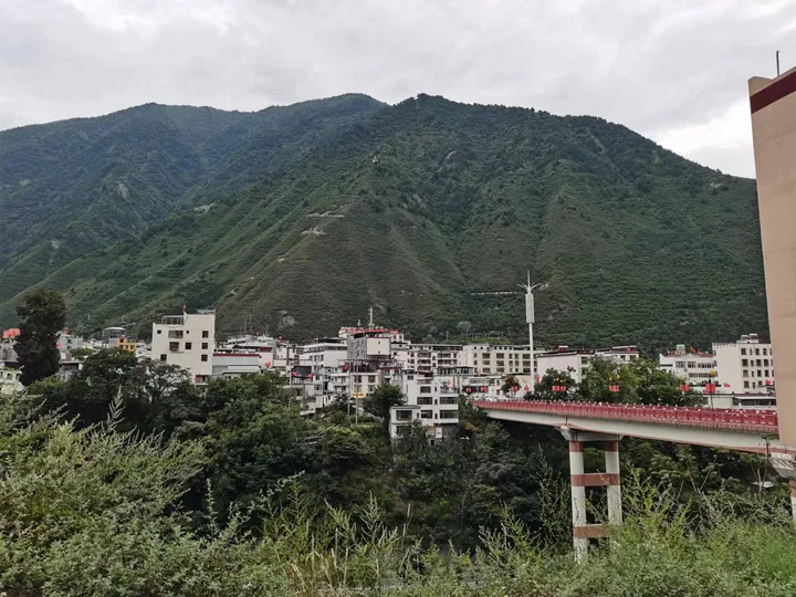A river town with a bridge, backed by green mountains, in Mao County