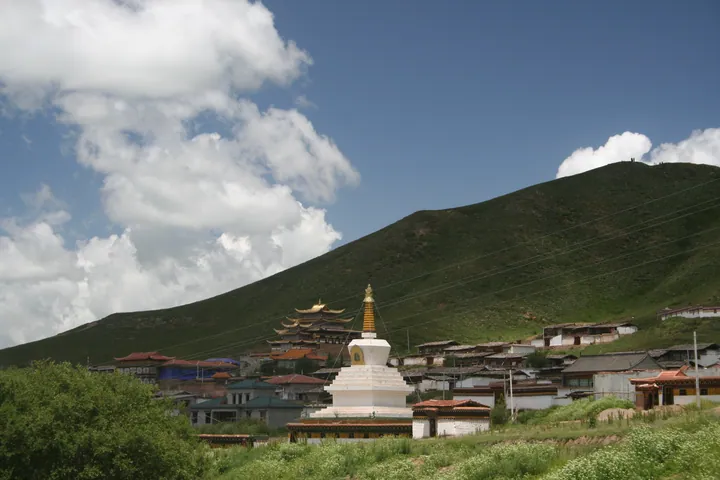 White stupa and monastery buildings below green hills in Tangke Township, Zoige County