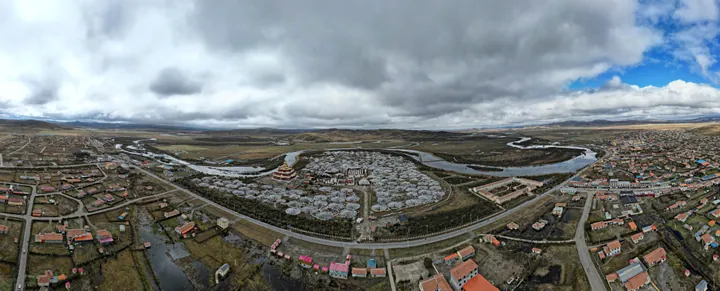 An aerial panorama of a circular Tibetan monastery complex on the grassland in Hongyuan County