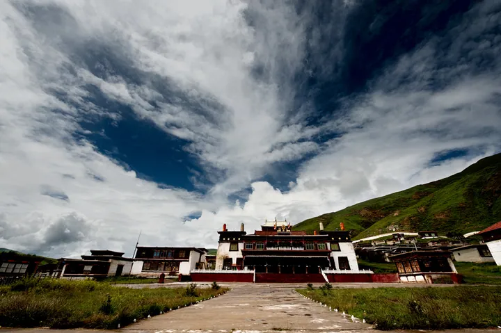 A Tibetan monastery building under a dramatic sky in Luhuo County