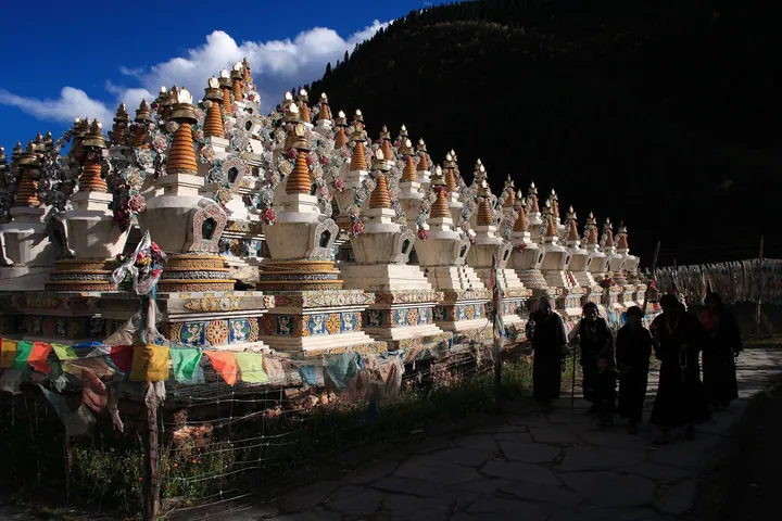 Rows of Tibetan Buddhist stupas with pilgrims walking past in Xinlong County