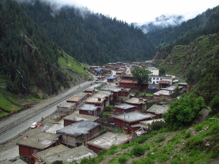 A small township with wooden-roofed houses in a misty forested valley in Dêgê County