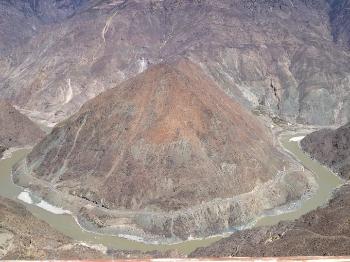 A U-shaped bend of the Jinsha River seen from an overlook, with a road along the canyon, Dêrong County