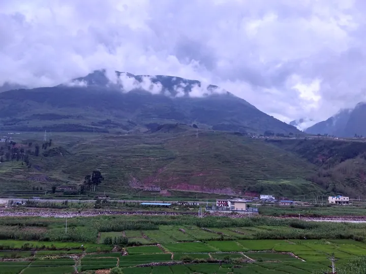 Rice paddies and village houses below misty mountains near Qiaowo Town, Puge County