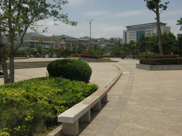 A paved town square with benches, hedges and low-rise buildings in Zhanyi District