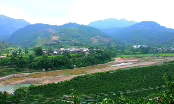 A river winding through farmland and a village below forested hills in Huaning County