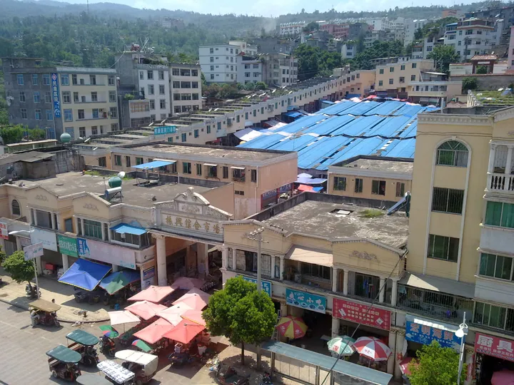 A covered market with blue roofing surrounded by multi-storey buildings on a hillside in Yongshan County