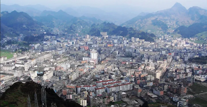 A hazy aerial view of a town filling a valley surrounded by green hills in Weixin County