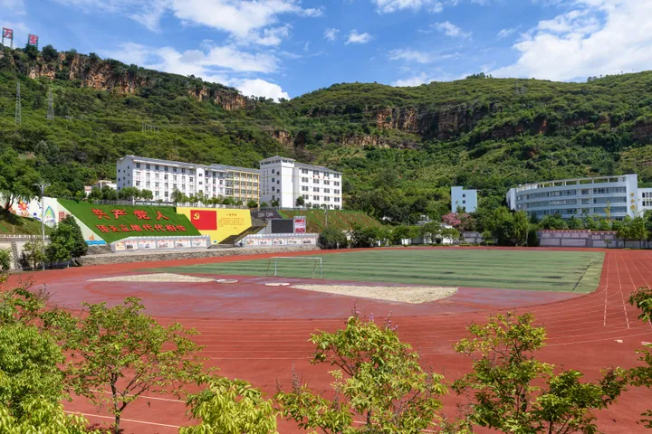 School sports field and buildings with mountains behind, Huaping County