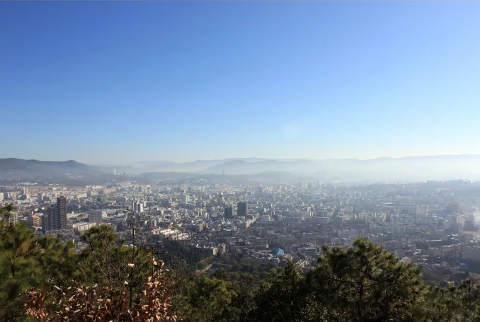 A hazy panoramic view of a city spread across a valley, seen from a hillside