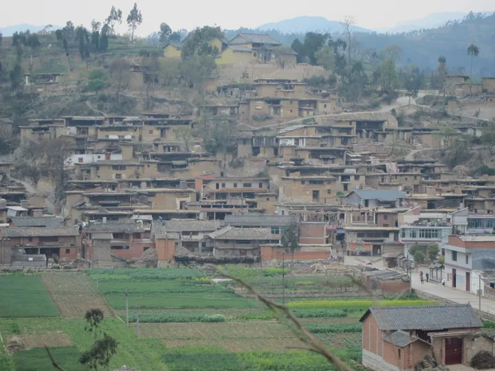 Hillside village of traditional mudbrick houses with terraced farmland in front, Luxi County