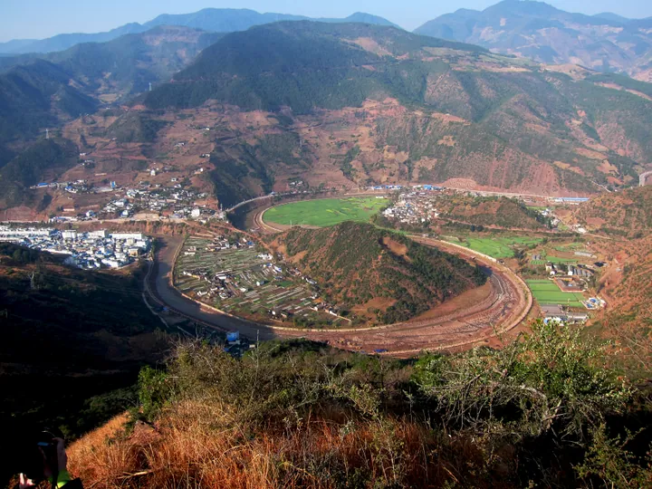 Aerial view of a horseshoe-shaped river bend with a hillside village, Yunlong County