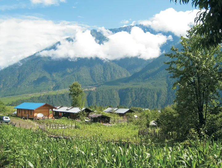 Wooden farm buildings and a cornfield beneath cloud-wreathed mountains