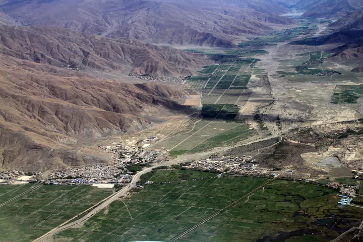 A hazy aerial view of a river valley with farmland and a village in Gonggar County, Tibet