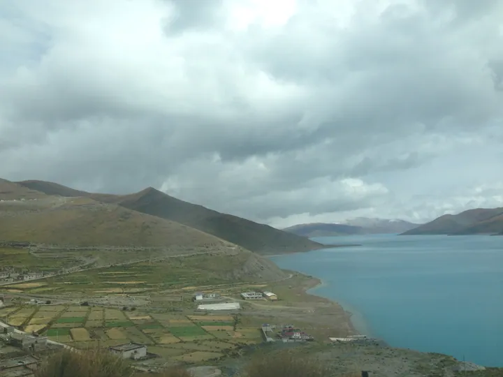 Turquoise lake with farmland and a village on its shore, Nagarzê County