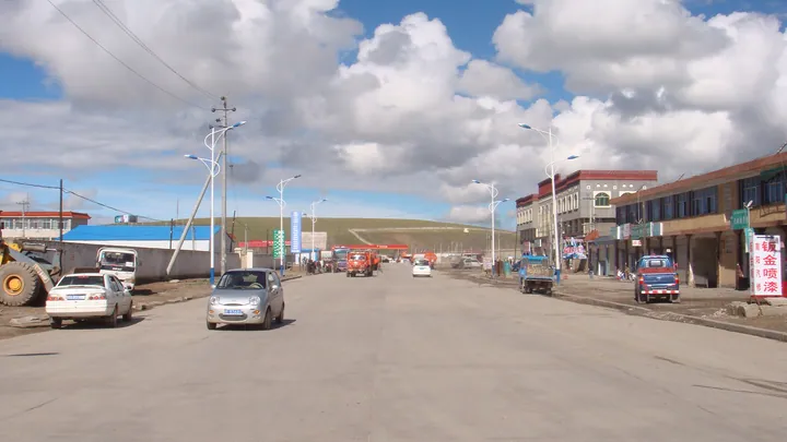 A wide street with shops and parked vehicles in Nagqu town