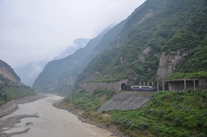 Mountain river gorge with a railway tunnel and train near Lueyang