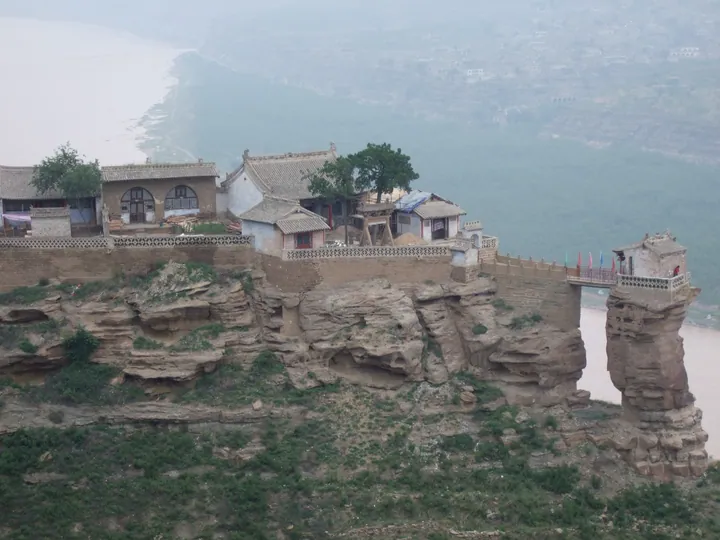 Temple buildings and a footbridge atop a sandstone cliff and rock spire overlooking the Yellow River in Jia County