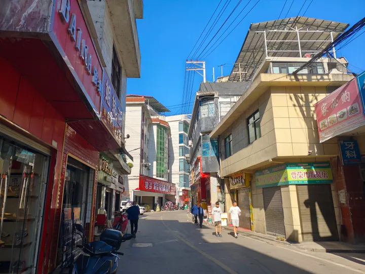 A sunny small-town street lined with shops and pedestrians in Maoba, Ziyang County
