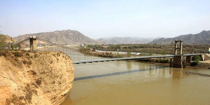 A suspension bridge crossing the Yellow River with mountains in the background