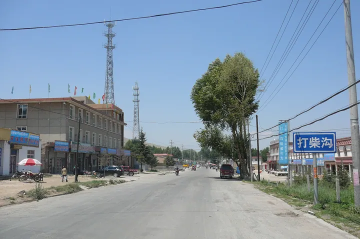 A small-town street with shops, a communications tower, and a road sign reading Dachaigou