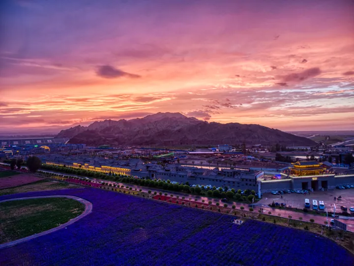 Colourful sunset sky over a lit scenic complex and fields in Linze County