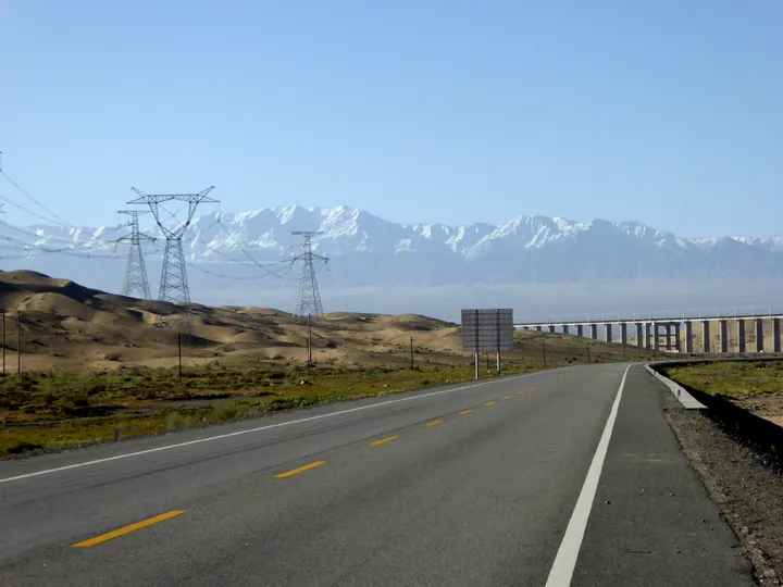 Snow-capped Altyn-Tagh mountains, sand dunes and a highway viaduct in Aksay Kazak Autonomous County
