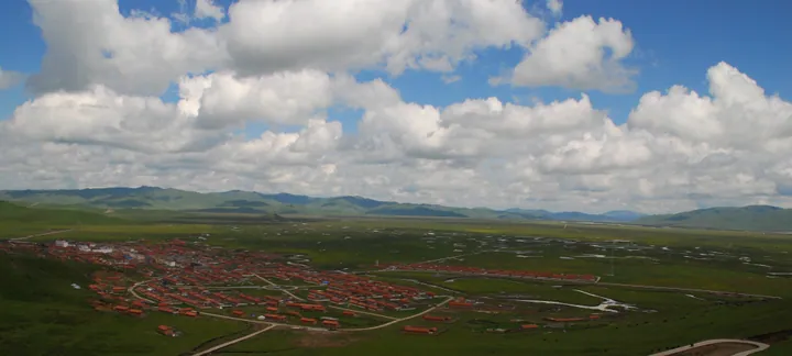 Red-roofed buildings of Awancang township amid green grassland and wetlands in Maqu County