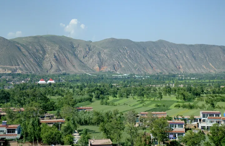 Farmland, trees and houses in a valley beneath bare hills in Haiyan County