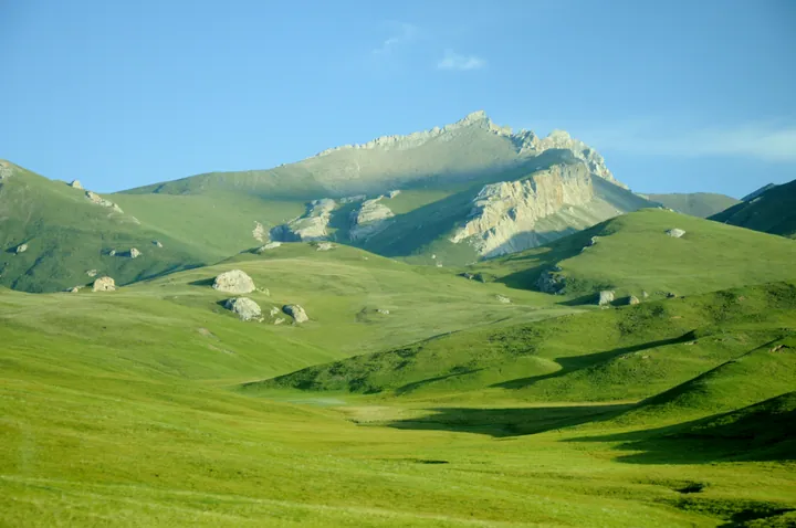 Green grassland below a rugged mountain peak in Tianjun County