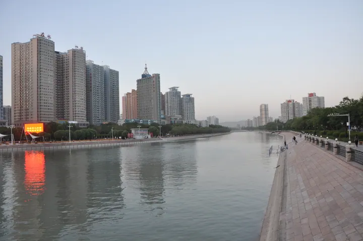 High-rise buildings reflected in the Konqi River at dusk in Korla