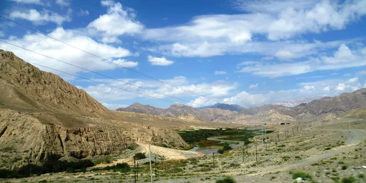 A river winding through an arid mountain valley under a blue sky with clouds