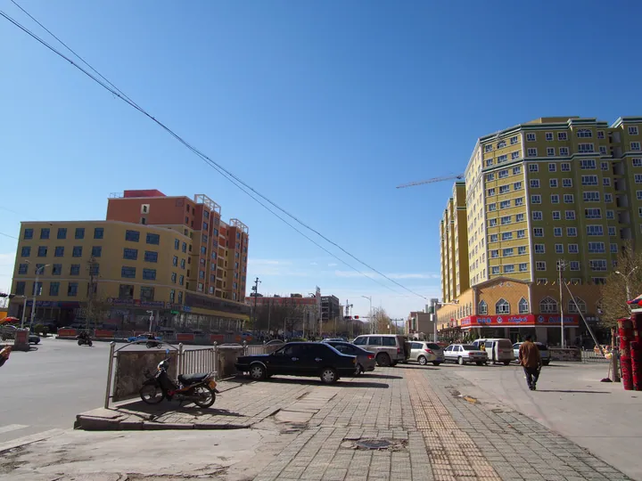 City street with multi-storey buildings, parked cars and a motorbike under a clear sky