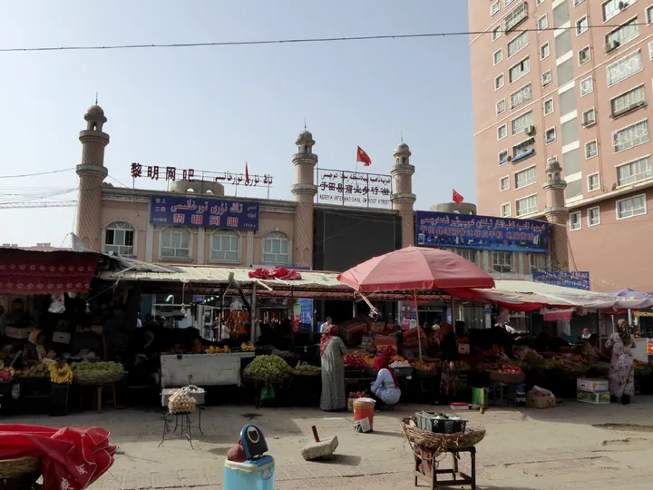 An open-air bazaar with stalls, produce and a mosque-style building in Yutian County