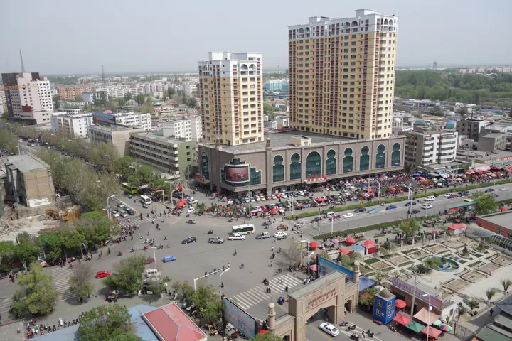 Elevated view of a busy city square with a large arched commercial building, traffic and pedestrians