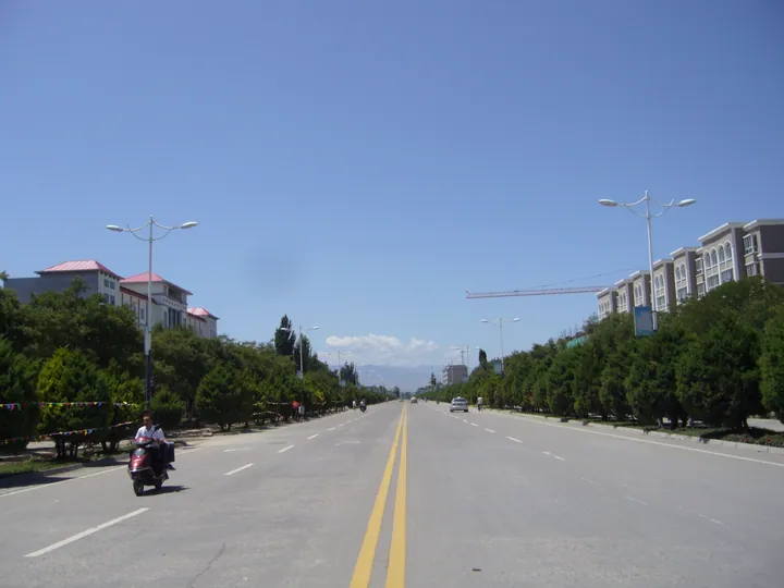 Wide street lined with trees, a motorbike rider, and mountains on the horizon