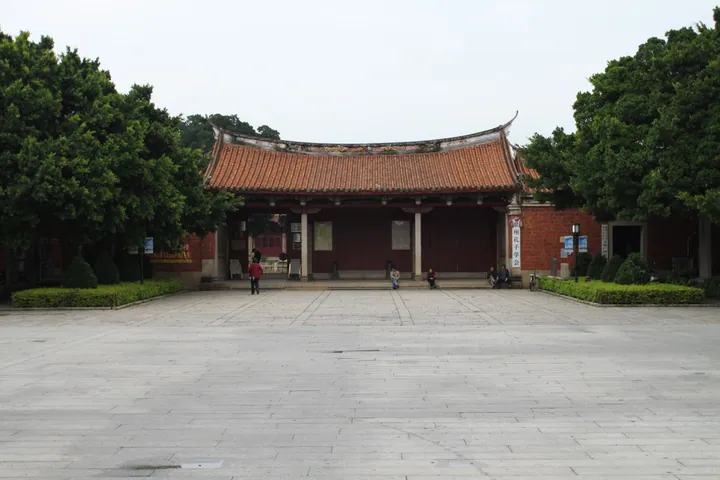 Traditional red-tiled temple hall with people seated in the forecourt