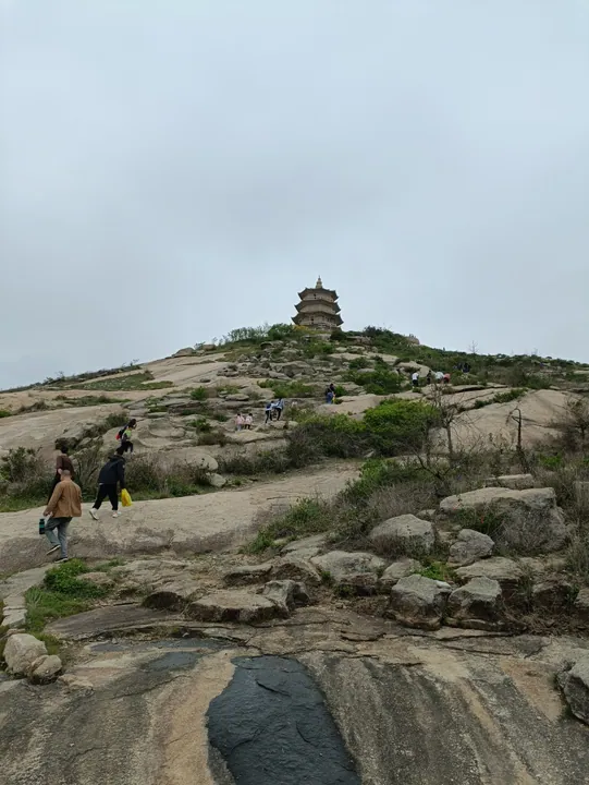 A tall stone pagoda atop a rocky hill with visitors on the path below