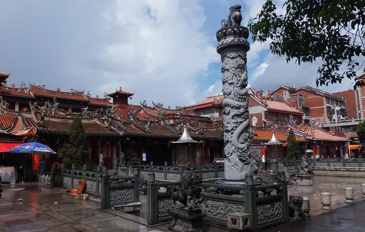 Temple courtyard with an ornately carved stone dragon pillar and painted rooflines