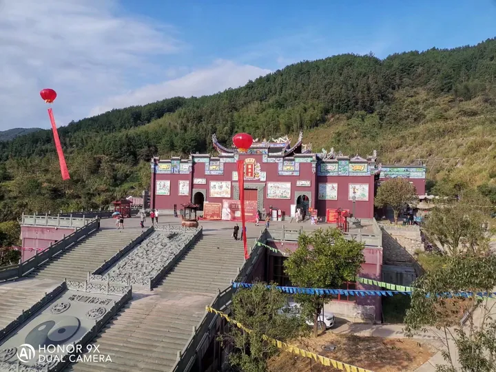 A red temple complex with a courtyard and staircase on a forested hillside