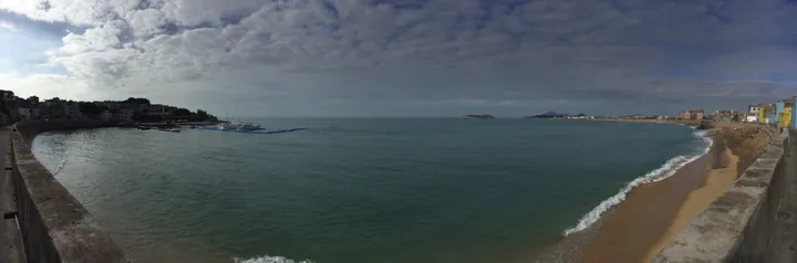 Wide panoramic view of a crescent-shaped bay with a sandy beach and coastal town