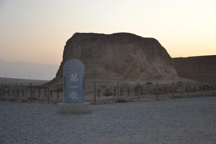 An eroded earthen mound behind an inscribed marker stone at dusk
