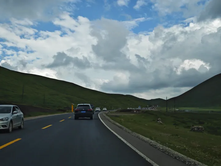 Green rolling grassland hills beside a highway in Sangke Grassland, Xiahe County, Gansu