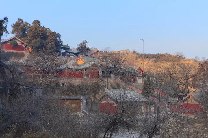 Cluster of red temple halls on a wooded hillside lit by evening sun