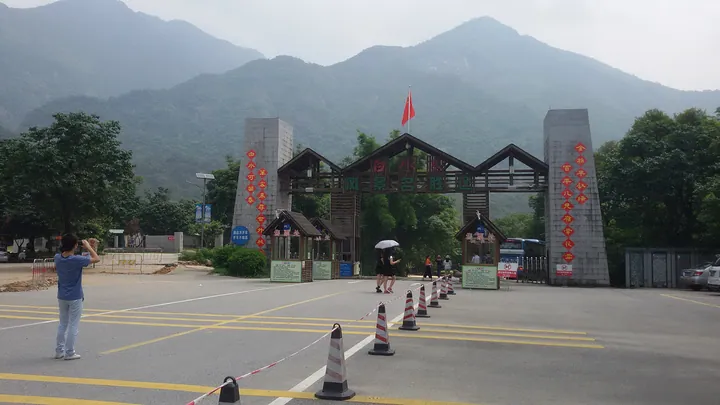 A wooden and stone gateway entrance with mountains rising behind it, and a parking area in front