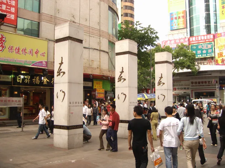 Stone pillars inscribed 'East Gate' at a busy pedestrian shopping street