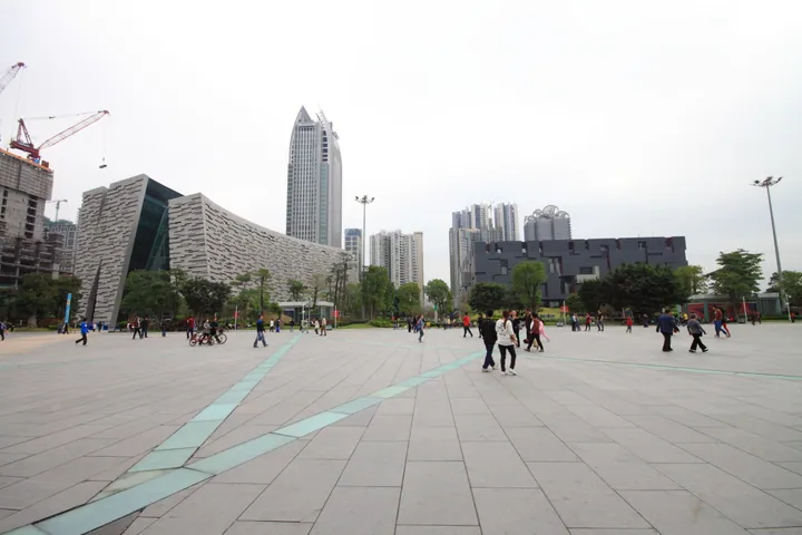 Wide paved plaza with modern museum and library buildings and skyscrapers in the background.